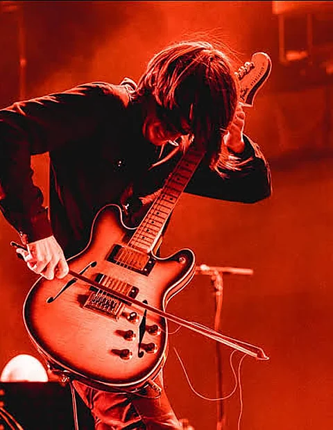 Guitarrista de Radiohead inclinado sobre su guitarra bajo una luz roja intensa